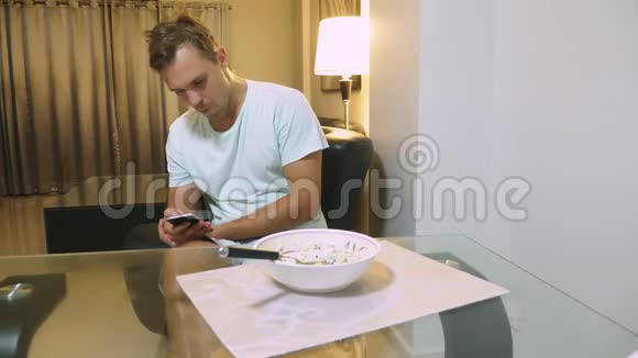 一个疲惫的人坐在客厅的桌子旁吃晚饭用电话视频的预览图