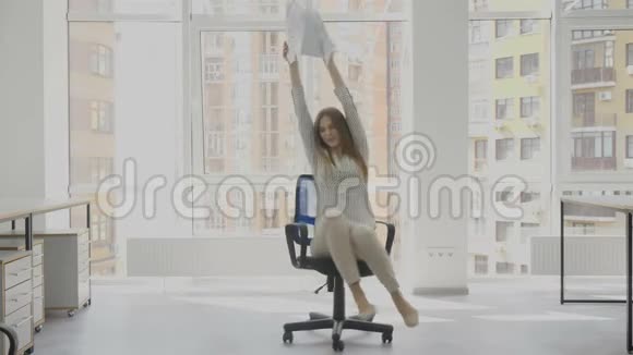 办公室工作人员年轻的女人坐在椅子上手里拿着文件快乐地在椅子上旋转着视频的预览图