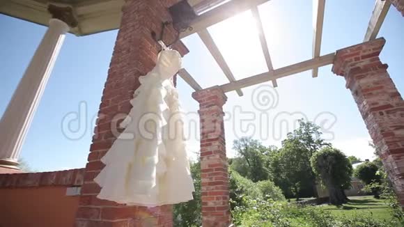 婚礼前一天一件白色的婚纱挂在红砖墙旁边阳光明媚视频的预览图