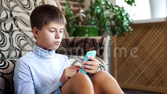 男孩坐在房间的地板上用智能手机现代技术在儿童生活中的理念视频的预览图