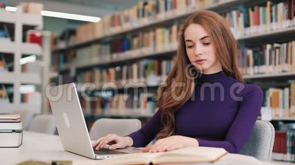 女学生拿着书和笔记本电脑坐在图书馆的桌子旁视频的预览图