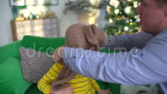 小父亲给小儿子穿上一件毛衣上面有雪花片驯鹿坐在家里的沙发上视频的预览图