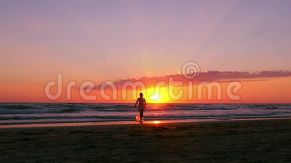 一个快乐的女孩在海浪和日落的背景下沿着海滩奔跑视频的预览图