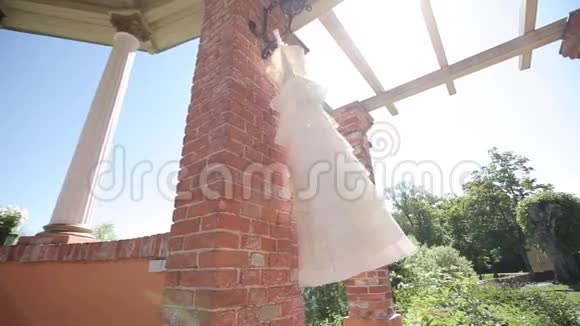 婚礼前一天一件白色的婚纱挂在红砖墙旁边阳光明媚视频的预览图