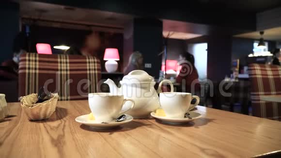 咖啡桌上有两个杯子和茶壶模糊的人背景咖啡厅内部4k视频的预览图