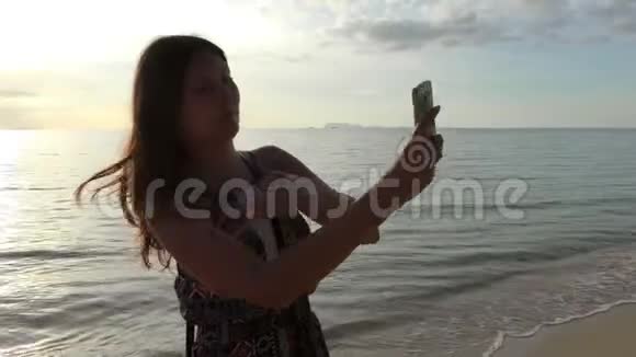 在日落或日出时在海滩上自拍的年轻美女视频的预览图