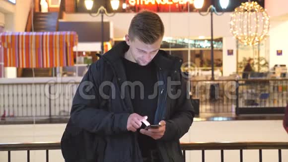 年轻人在购物中心使用智能手机在智能手机上浏览信息和滚动图片的人正面观点视频的预览图