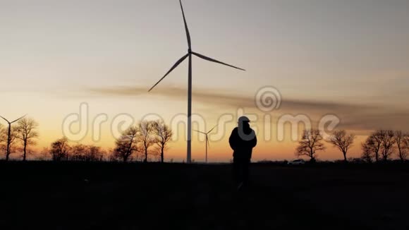 一个人的剪影沿着风力涡轮机的方向走向日落视频的预览图