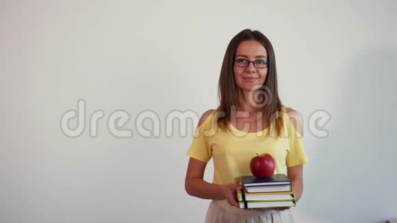 白色背景的年轻教师肖像上面有一叠书和苹果的女孩视频的预览图