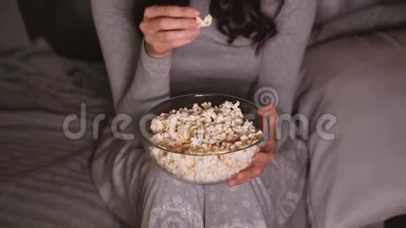 漂亮的女人在家里看电视上有趣的东西吃爆米花视频的预览图