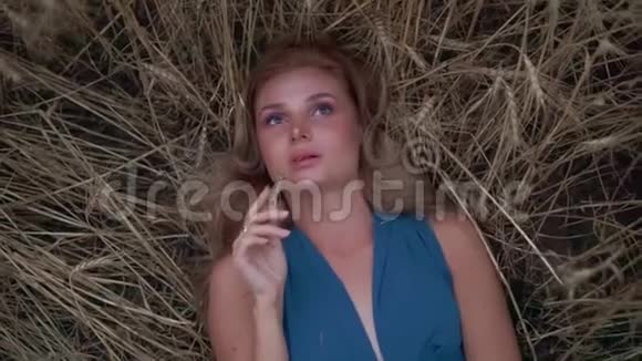 漂亮的年轻女子躺在金色的麦田里她的手在摸麦穗收获概念收获视频的预览图