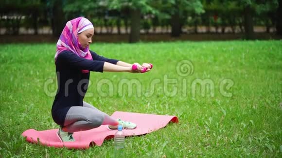 一位戴着面纱的现代穆斯林妇女在夏日在公园里做运动视频的预览图