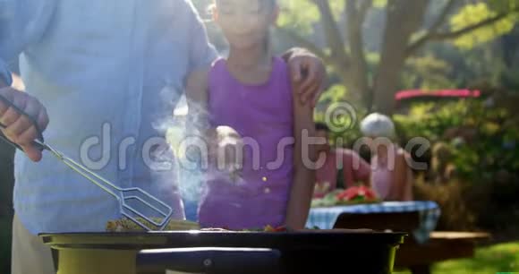 祖父和孙女正在准备烧烤而家人正在用餐视频的预览图