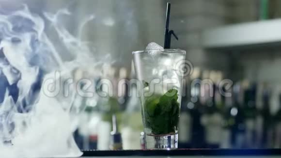 酒精鸡尾酒冰块和绿色叶子大玻璃黑色塑料吸管站在酒吧的桌子上薄雾视频的预览图