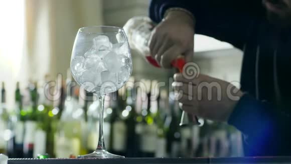 酒吧工作人员将威士忌加入到杯子中在桌子上在没有重点的瓶子背景上贴上冰块视频的预览图