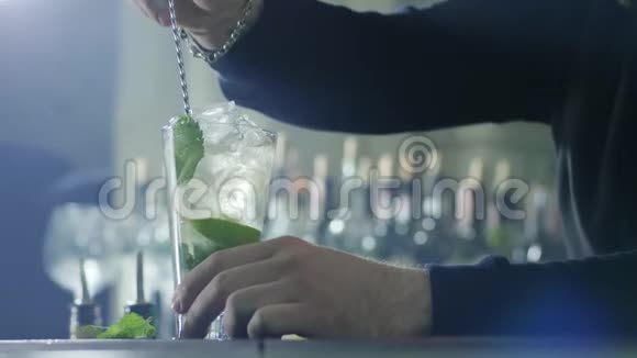 男人手里拿着一把勺子银手镯把鸡尾酒和冰块混合在一起大玻璃杯里放着绿色的薄荷叶视频的预览图