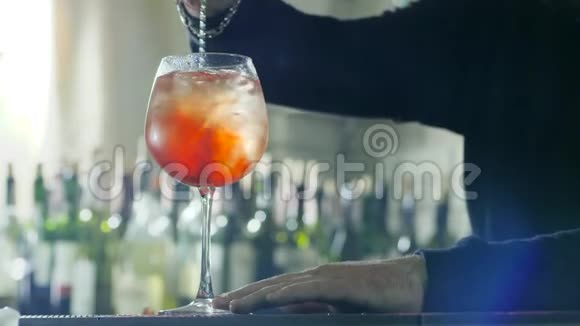 酒吧服务员手里拿着长长的金属勺子把五颜六色的鸡尾酒和冰和威士忌放在桌子上的玻璃里视频的预览图