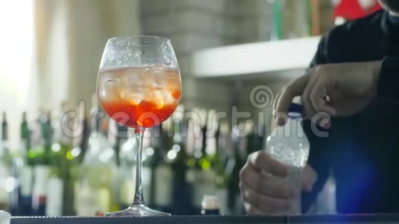 工作中的酒保可以做提神饮料并在酒杯中加入含冰和干邑的碳酸矿泉水视频的预览图