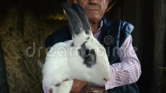 一个戴草帽的老农正在抱一只大白兔干草背景下男人的肖像视频的预览图