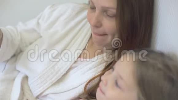 一个小女孩和妈妈躺在床上看着智能手机屏幕上的卡通片儿童和数字视频的预览图