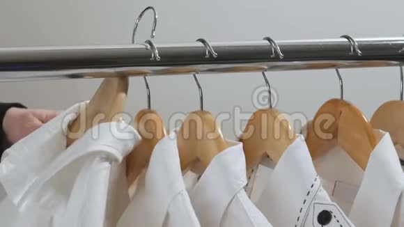 穿黑色夹克的女人会选择挂在衣柜或商店衣架上的白色衬衫视频的预览图