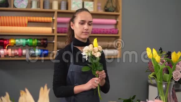 年轻的花艺师在鲜花店布置现代花束的慢镜头她把奶油玫瑰和黄色结合在一起视频的预览图
