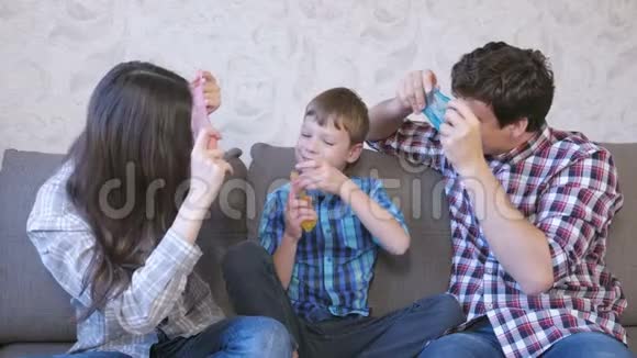 快乐的家庭妈妈儿子和爸爸玩泥浆坐在沙发上从黏液里看过去视频的预览图