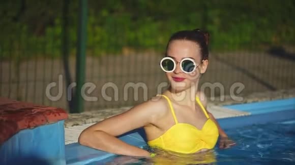 一个在游泳池里喝凉水的年轻女子在夏天放松视频的预览图
