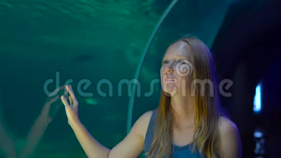 一名年轻女子从水族馆的管道里走进来在一个背景下用一束光看鱼视频的预览图