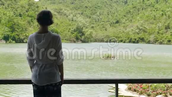 年轻女子站在背景的河流和山上覆盖着绿色的森林看河和青山的女孩视频的预览图