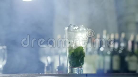 酒吧老板的手把塑料吸管放进清爽的鸡尾酒里冰块和绿叶放在玻璃里站在酒吧里视频的预览图