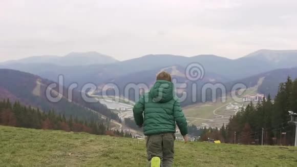 一个穿着绿色衣服的男孩沿着高山奔跑晴朗的秋日视频的预览图