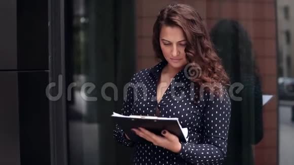年轻有魅力的商务女性正在考虑在办公楼旁边的文件中进行商务项目视频的预览图