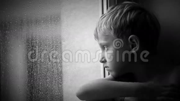 一个小男孩透过窗户透过玻璃看雨滴视频的预览图