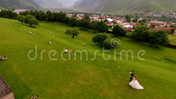 结婚新娘和新郎在群山的映衬下沿着绿草奔跑视频的预览图