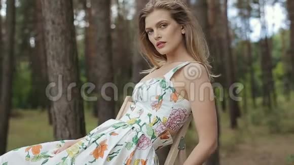 美丽的女孩穿着有趣的衣服坐在靠近森林的椅子上对着镜头摆姿势视频的预览图