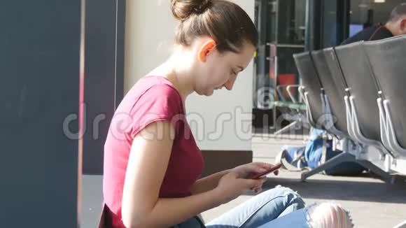 年轻女子在机场候机厅使用智能手机有智能手机的女孩在候机厅等待飞行视频的预览图