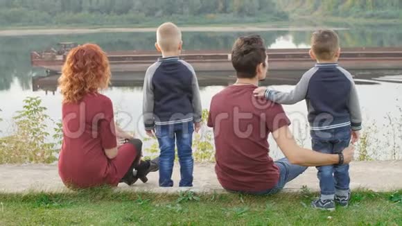 家庭和儿童的概念年轻夫妇和两个儿子在河边散步视频的预览图