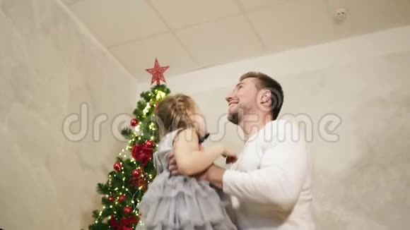年轻的父亲把他可爱的女儿扔在家里的空气中背景是装饰好的圣诞树她是视频的预览图