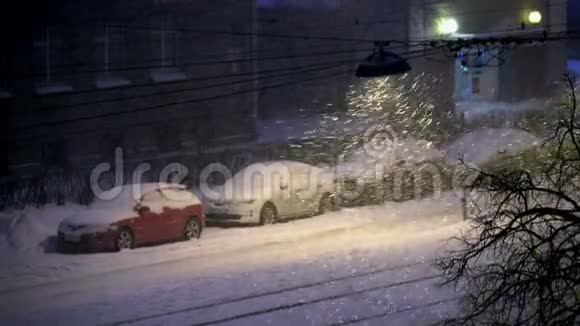 白雪覆盖的汽车在城市里夜幕下的大雪在城市里点燃了路灯视频的预览图