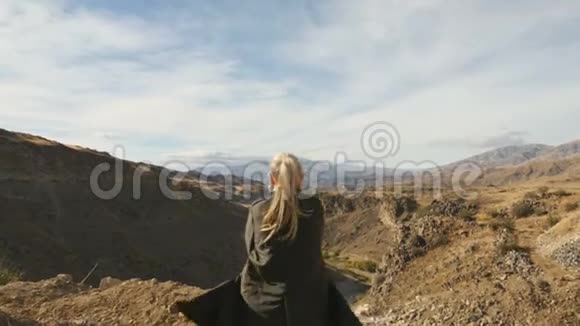 年轻女子站在悬崖边举起双手迎着高高的岩石山在那里晒太阳视频的预览图