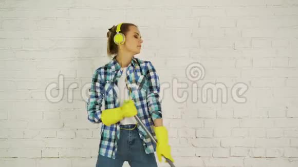 一位带着耳机和拖把的年轻女子准备回家打扫卫生为美妙的音乐跳舞唱歌视频的预览图