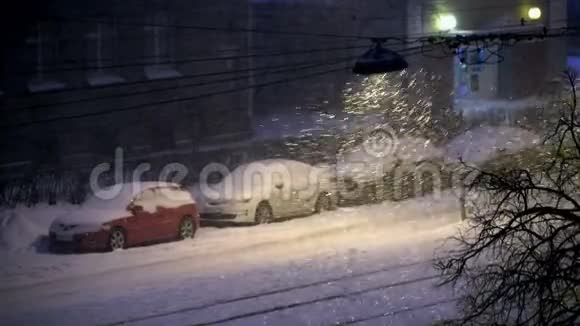 白雪覆盖的汽车在城市里夜幕下的雪在城市里点燃了路灯视频的预览图