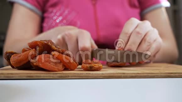一位年轻的家庭主妇用一把刀在砧板上切果干杏子健康饮食观念视频的预览图
