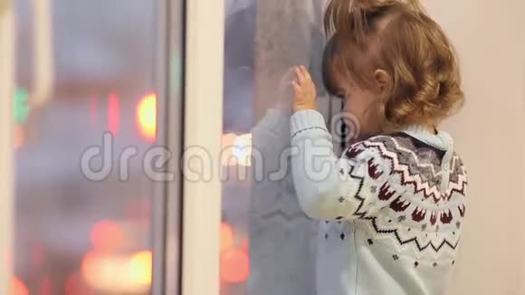 冬天一个小女孩站在窗台上透过窗户看过往的汽车视频的预览图