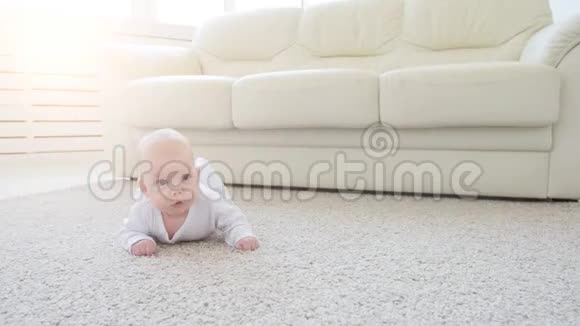 快乐的婴儿躺在地毯背景下微笑着穿着白色衣服的婴儿女孩视频的预览图