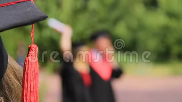 戴学术帽的女士看着快乐的朋友毕业后在公园里玩得开心视频的预览图
