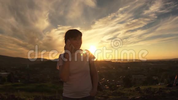 夏天日落时分黑发女人站在山上打电话视频的预览图