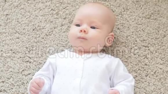 快乐的婴儿躺在地毯背景下微笑着穿着白色衣服的婴儿女孩视频的预览图