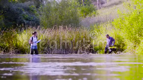 两位科学家穿着高橡皮靴在森林河的水中行走视频的预览图